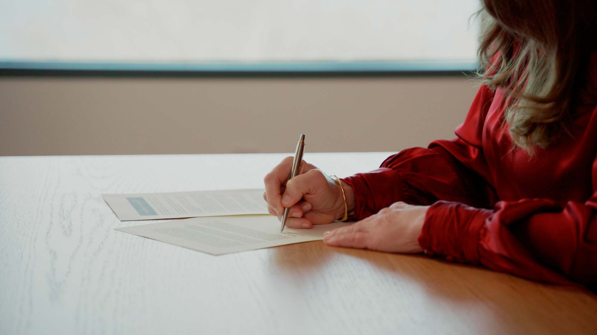 Melinda French Gates sits at a table and signs a piece of paper.