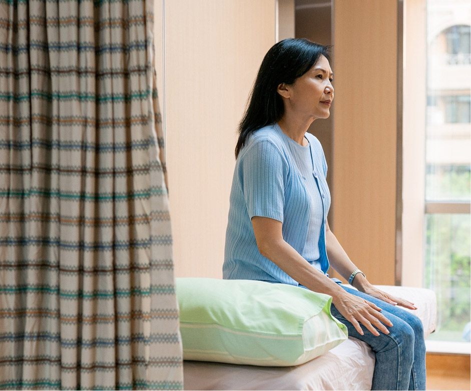 A woman sits on an exam bed in a hospital exam room.