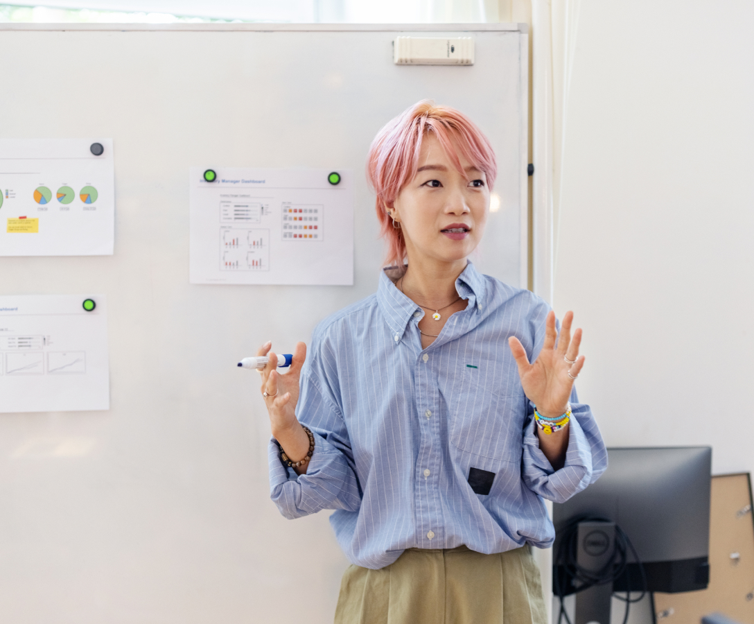 A woman presents new ideas to her team in front of a whiteboard.